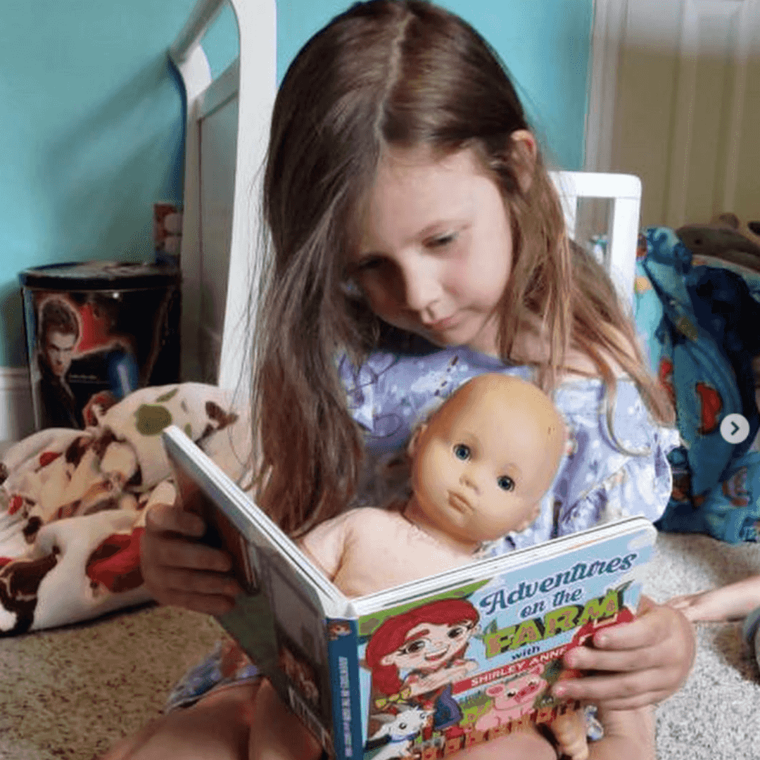 Young girl reading 'Adventures on the Farm: Children's Counting Book' to a baby doll, promoting early learning and counting skills for ages 0-5.